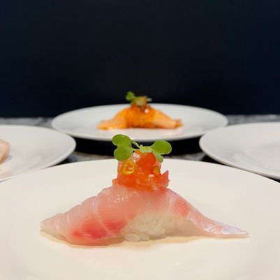 Sushi rolls topped with translucent fish slices and orange roe on white plates against a dark background