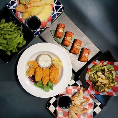 Assorted sushi and Japanese appetizers arranged on patterned plates around dipping sauces on a dark table