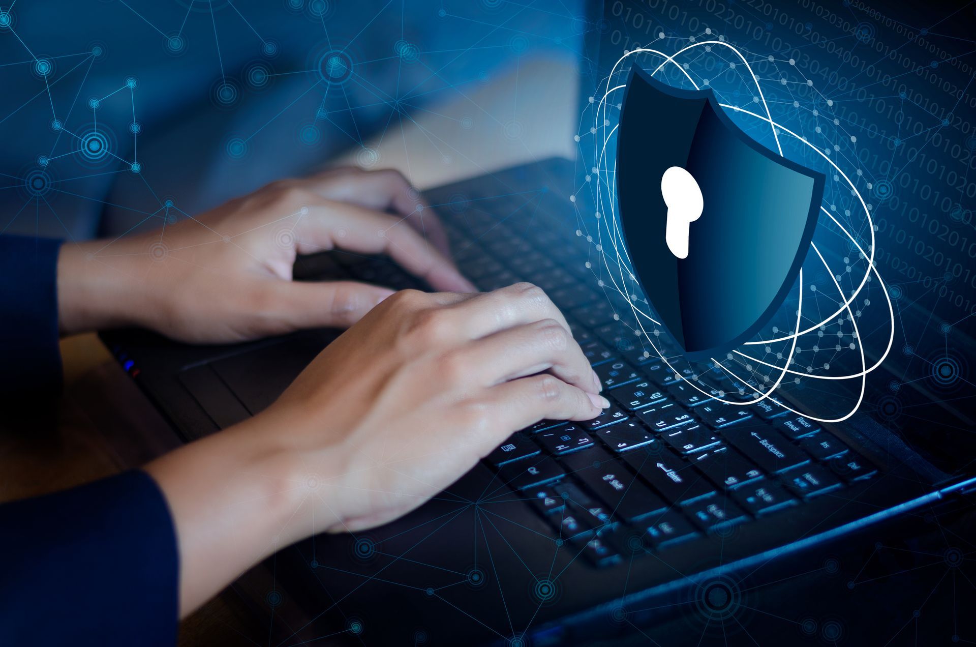 Hands typing on a laptop with a glowing security shield icon over a blue digital background