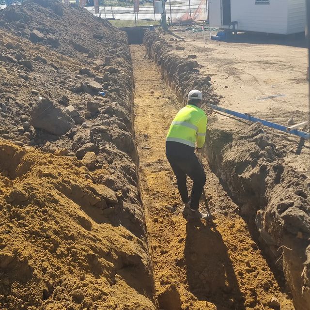 A man in a yellow shirt is digging a trench in the dirt