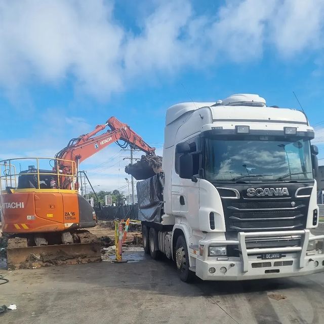 A white scania truck is parked next to an orange excavator