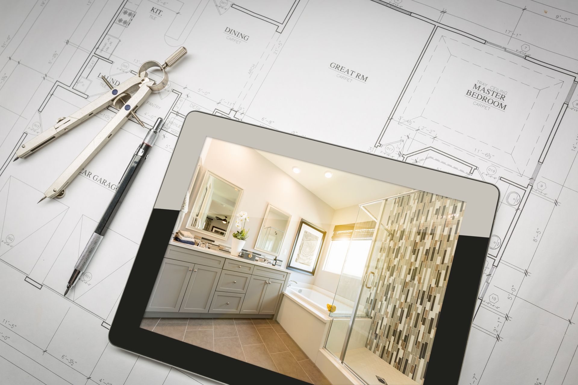 Tablet showing a bathroom design on top of home blueprints with tools beside it.