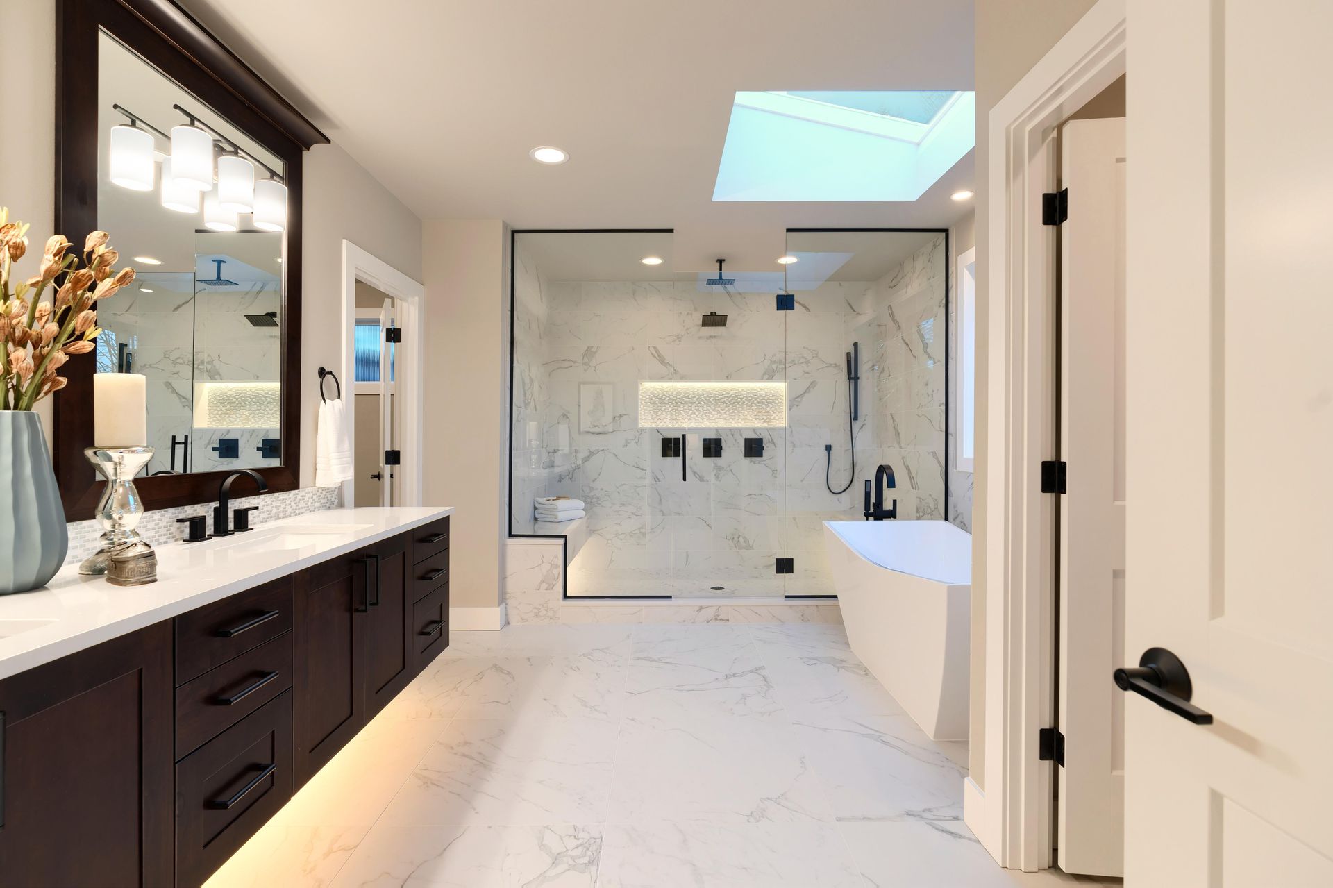 Bathroom remodeling with marble tile, glass walk-in shower, freestanding tub and dark vanity.
