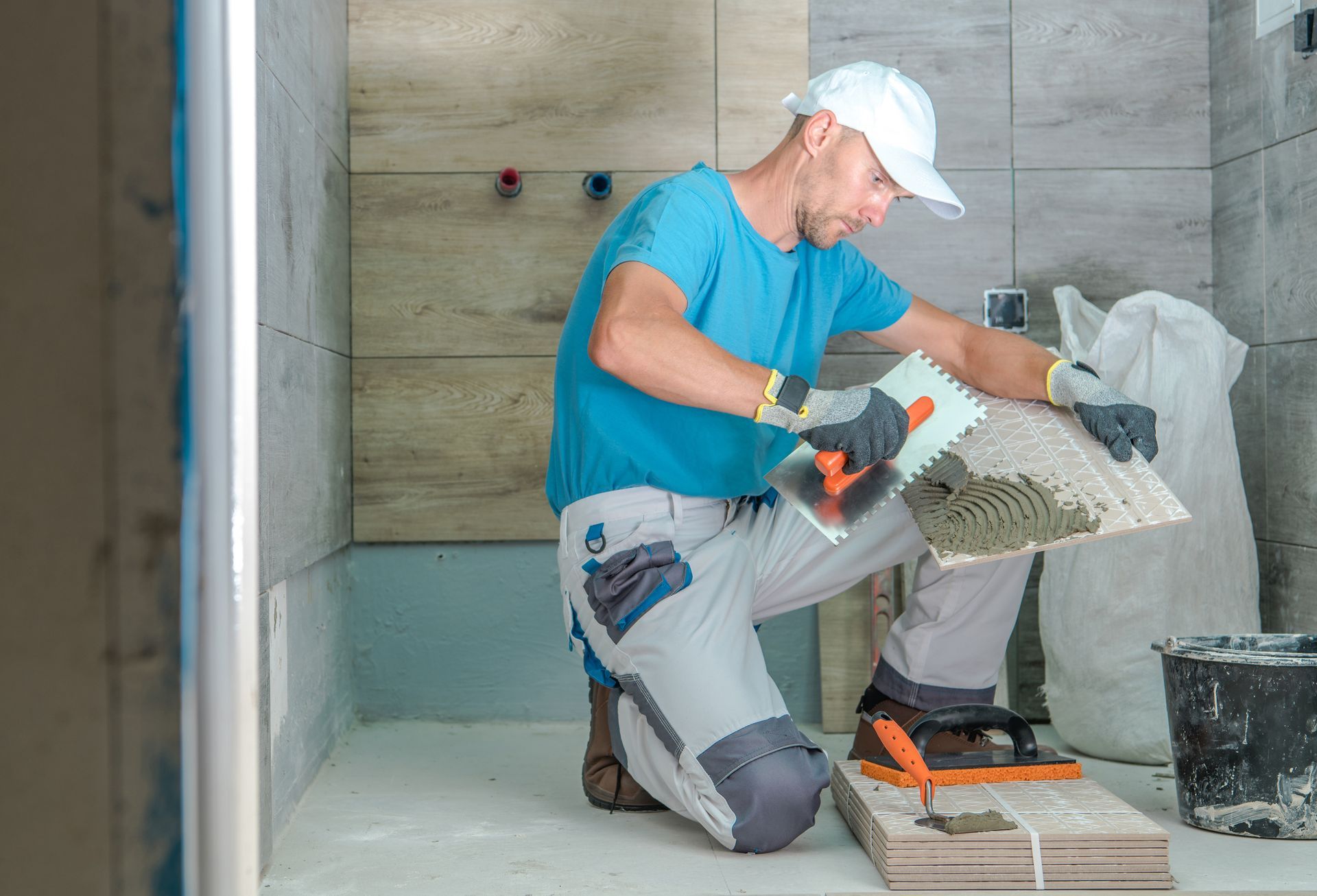 Man installing drywall around bathroom plumbing during a remodel Contractor applying adhesive to wall tile during a bathroom remodeling project.