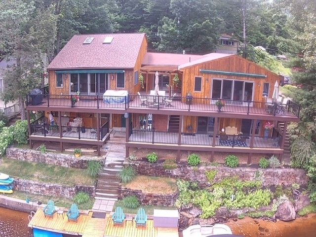 A multi-level wood deck wraps a lakefront home with railings, seating, and a dock below.
