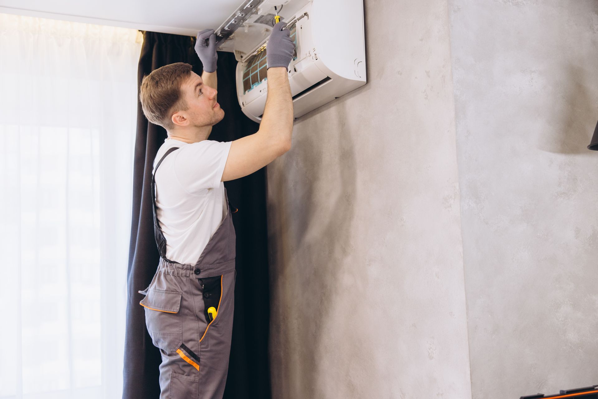 An air conditioning contractor repairing an air conditioner unit on the wall. An air conditioning contractor repairing an air conditioner unit on the wall.