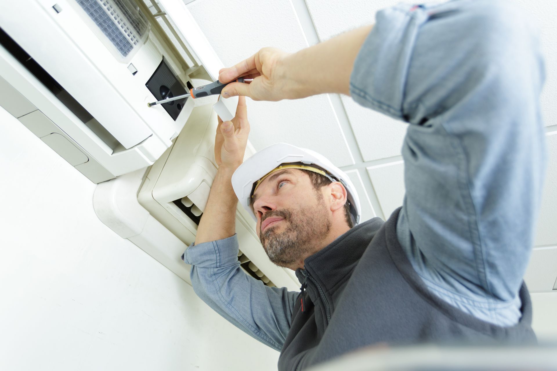 Air conditioning contractor servicing a wall-mounted AC unit indoors.