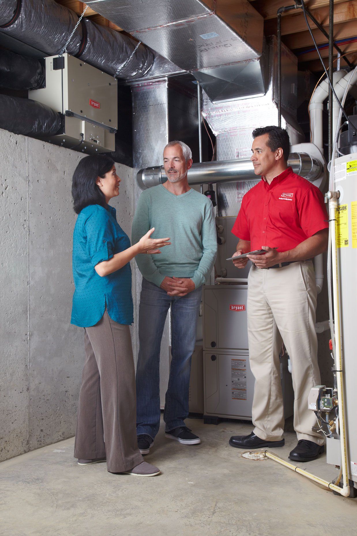 A technician in a red shirt consults with a couple in a utility room.