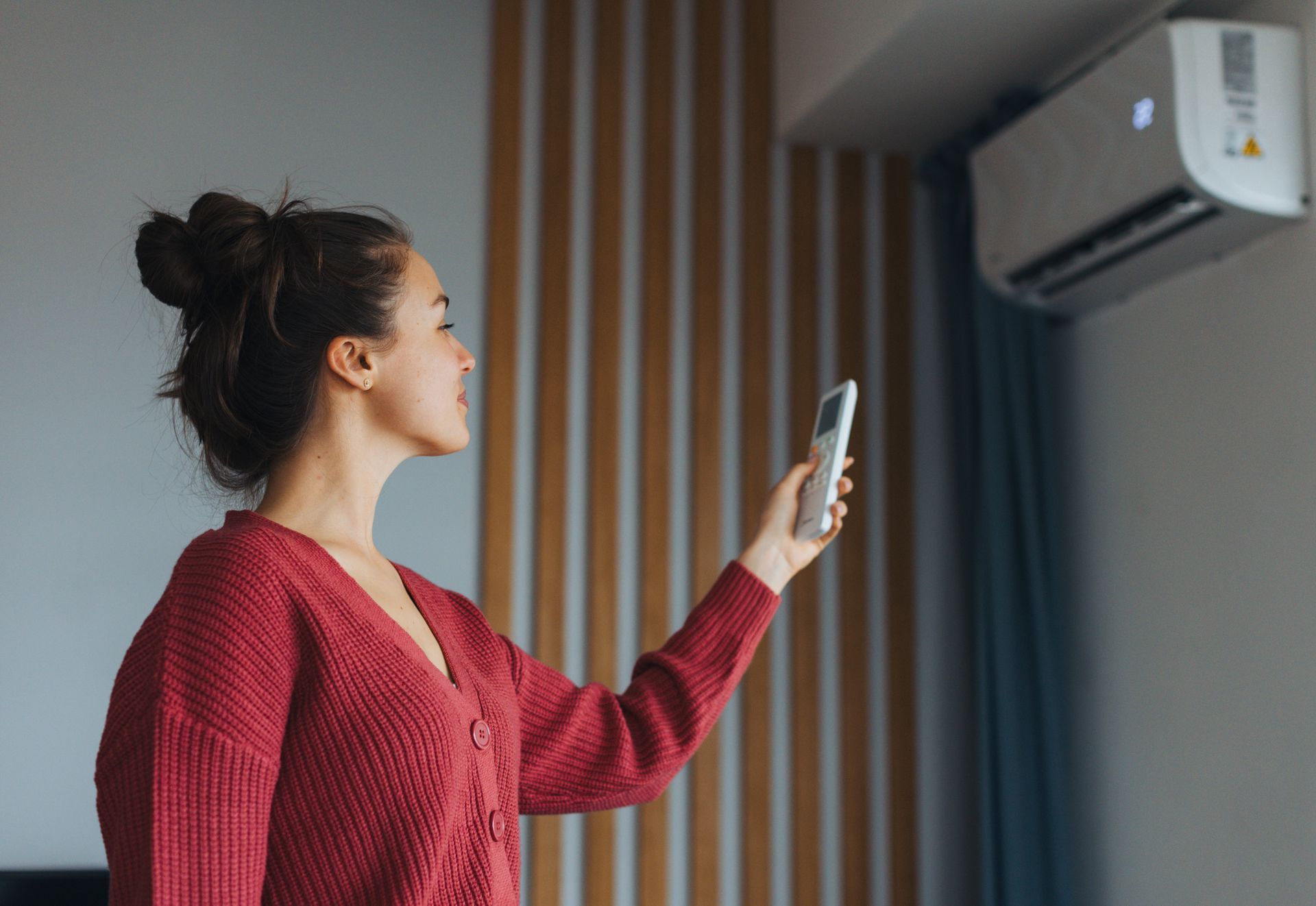 Woman adjusting temperature, holding remote controller.