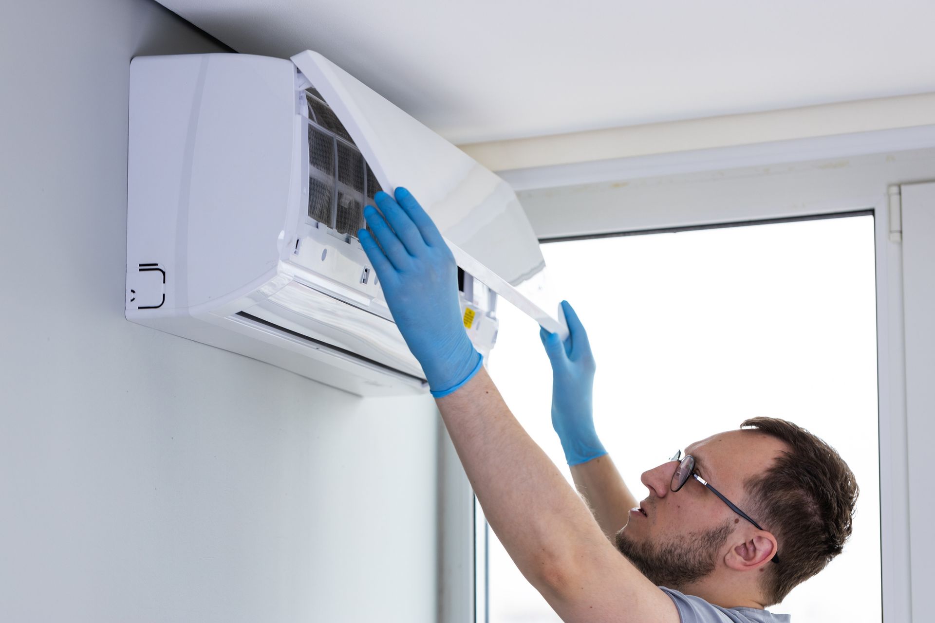 A technician in blue gloves installing a wall-mounted air conditioner unit indoors