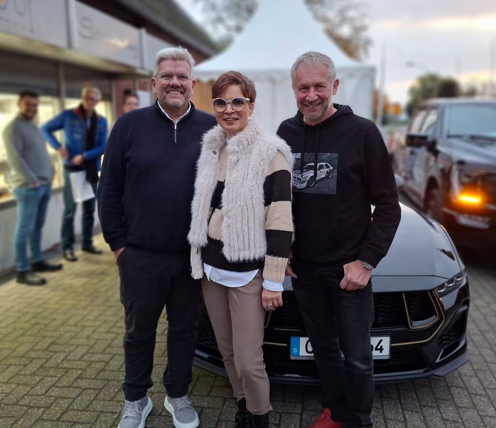 Drei Personen posieren für ein Foto vor einem schwarzen Auto