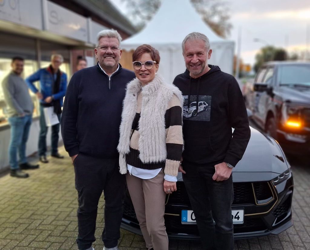 Drei Personen posieren für ein Foto vor einem Mustang
