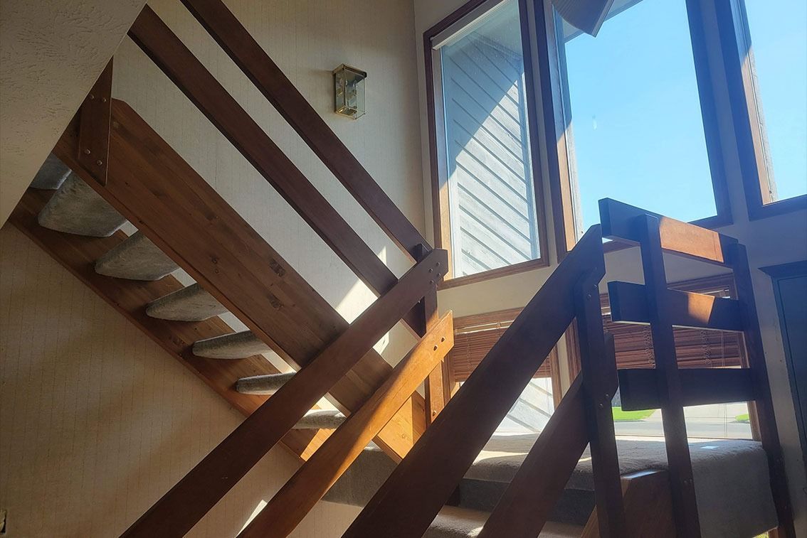 Wooden staircase inside a sunlit room with a window and blue sky outside