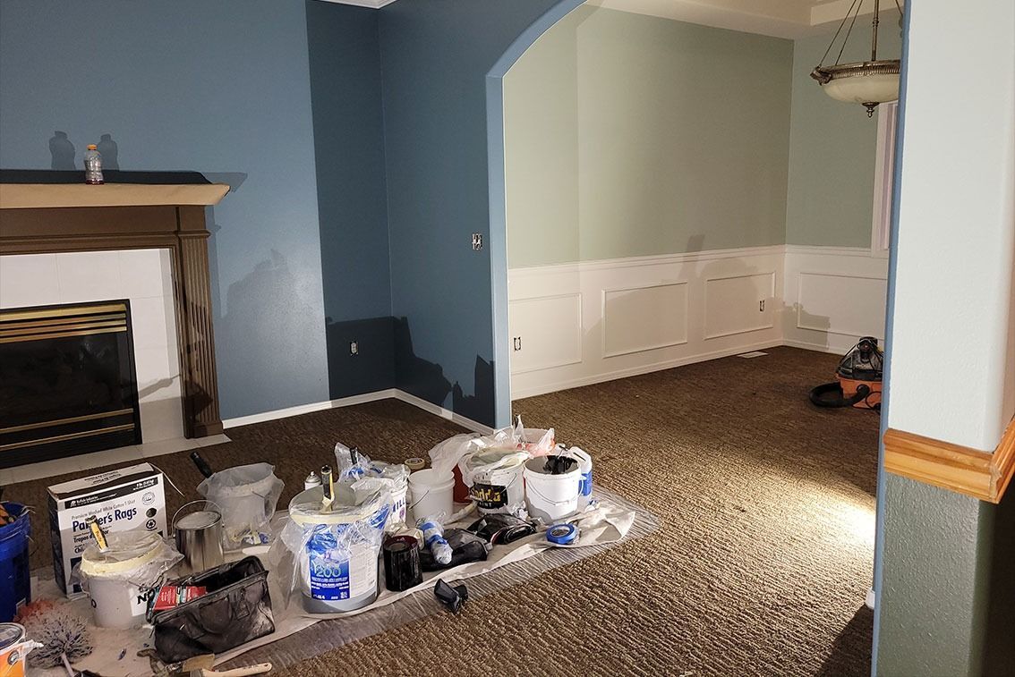 Empty room with blue walls, fireplace, and paint supplies on the carpeted floor