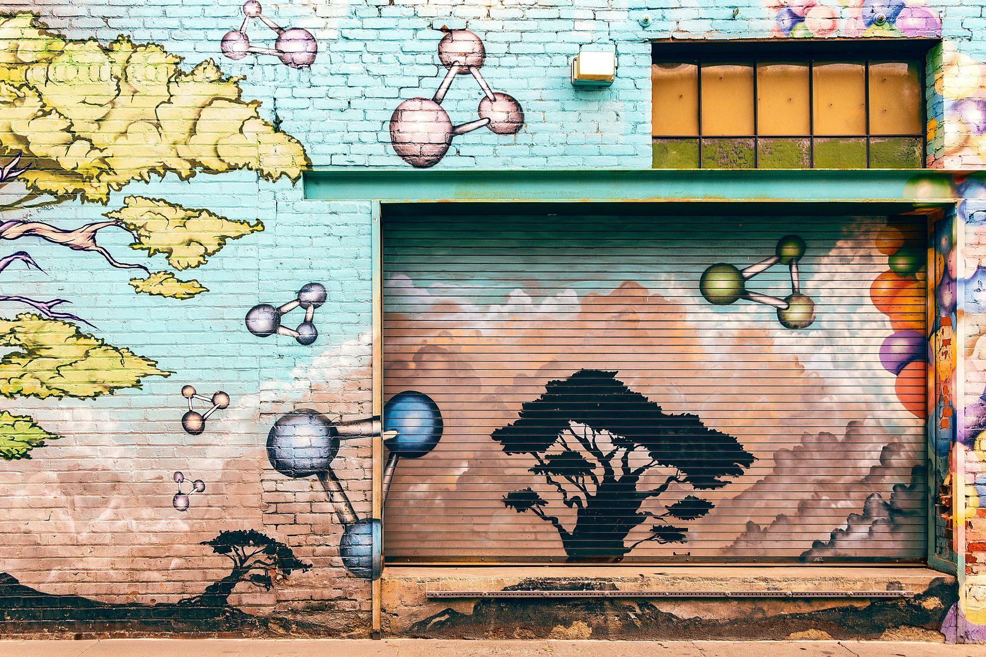Colorful mural of a tree silhouette, bubbles, and clouds painted on a brick wall with a window.