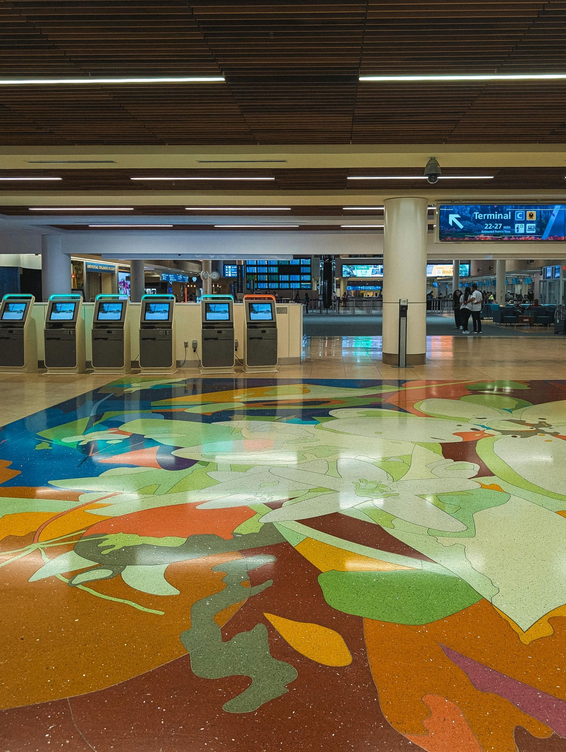 Airport terminal with colorful mosaic floor and self-service check-in kiosks in the background