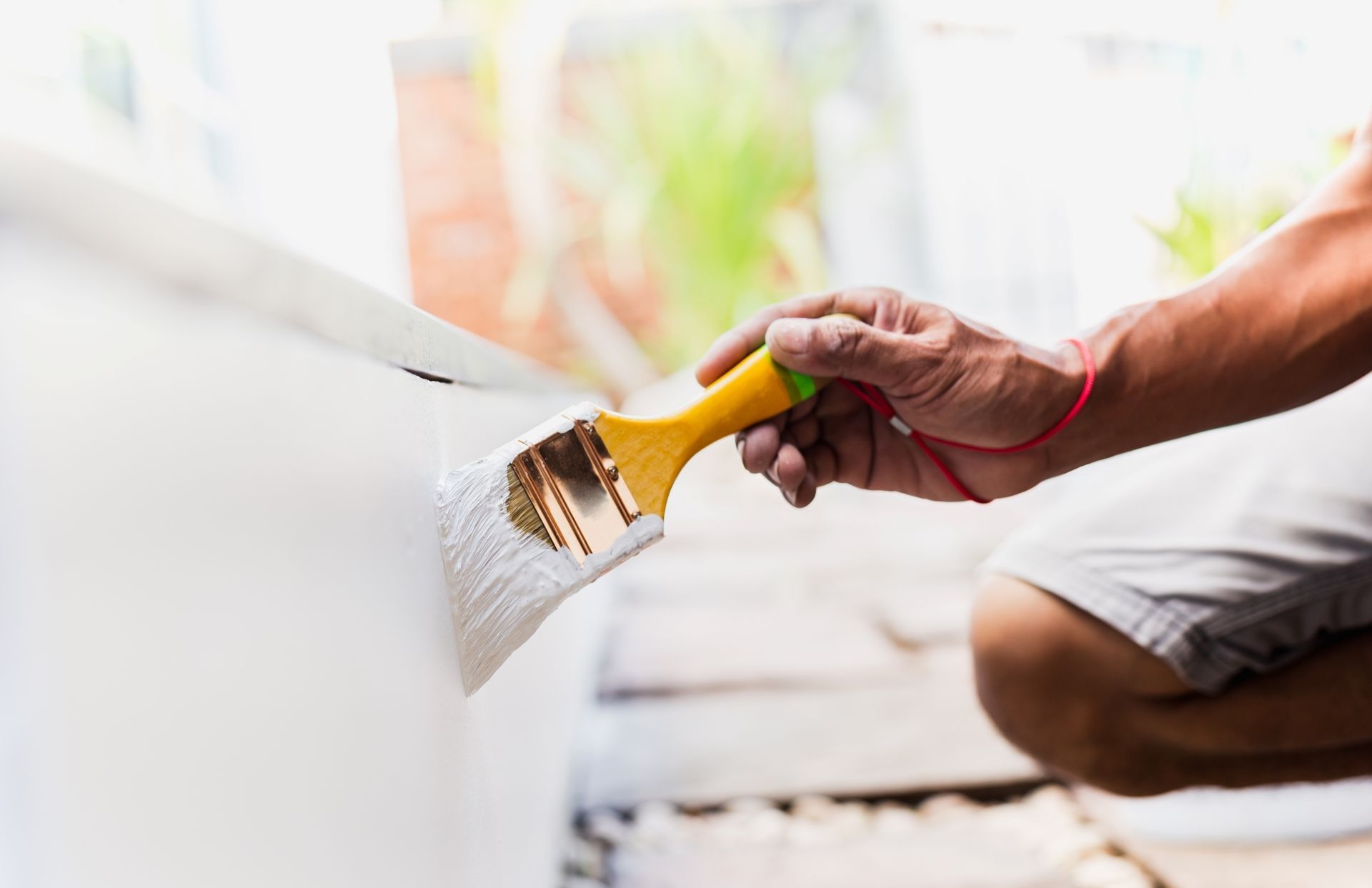 Painting a white surface with a yellow-handled brush while crouching nearby