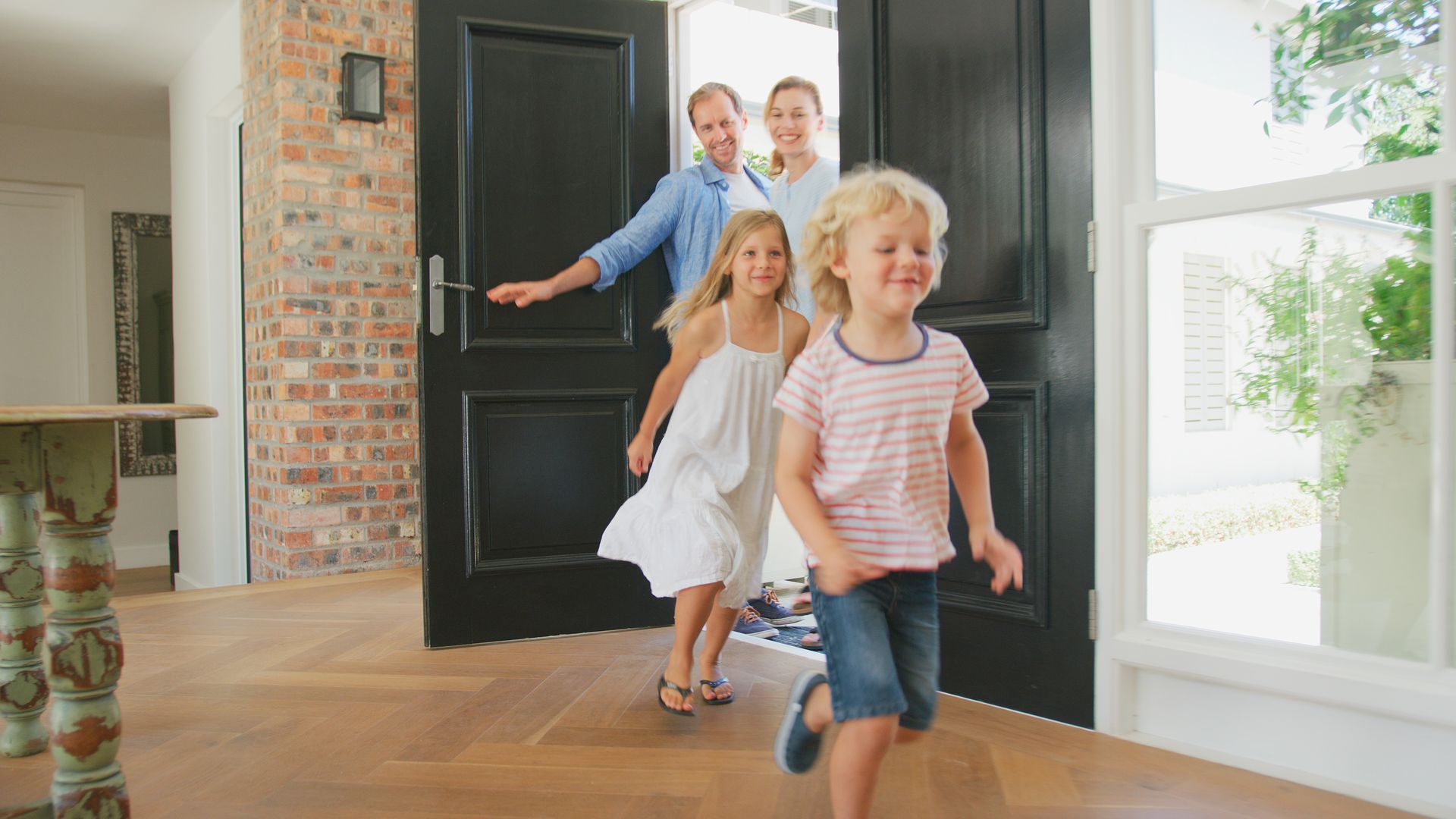 Family, 2 parents and 2 children, running through a doorway, smiling, bright light, wooden floor.