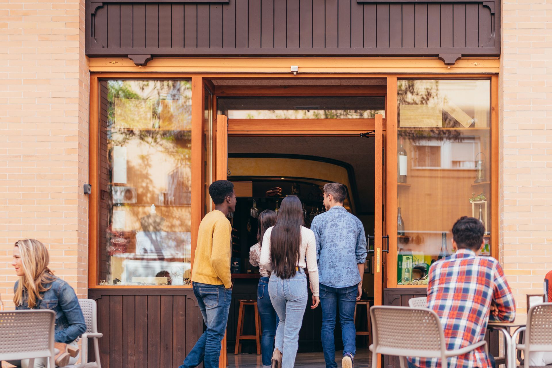 People entering a cafe with glass doors; a few seated outside on the patio.
