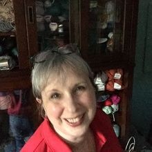 Smiling person in a red jacket indoors, with a dark wooden cabinet behind them