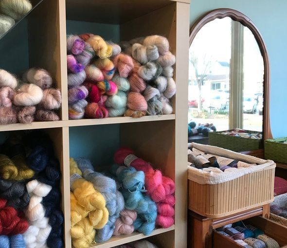 Shelves of colorful yarn skeins beside a mirror and basket in a cozy craft shop