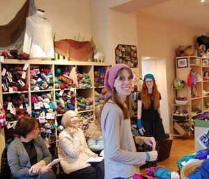 People chatting in a colorful craft shop, with yarn shelves and hats on display.