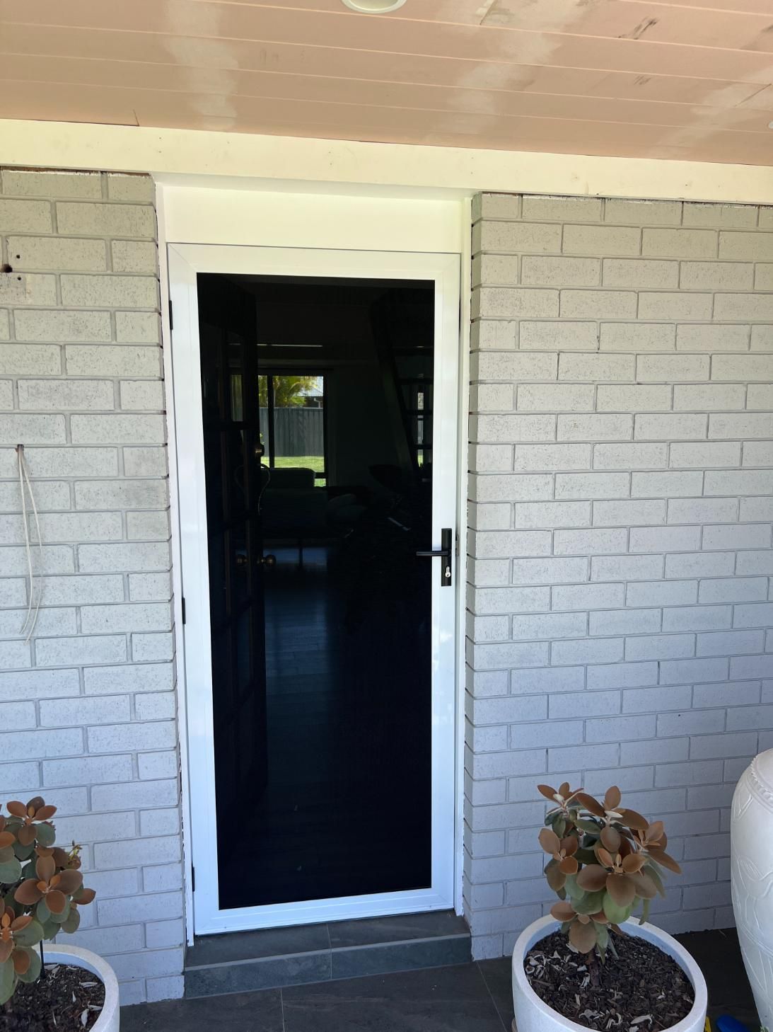 A White Brick House With A Screen Door And Potted Plants In Front Of It — Glass 24/7 In Taree, NSW