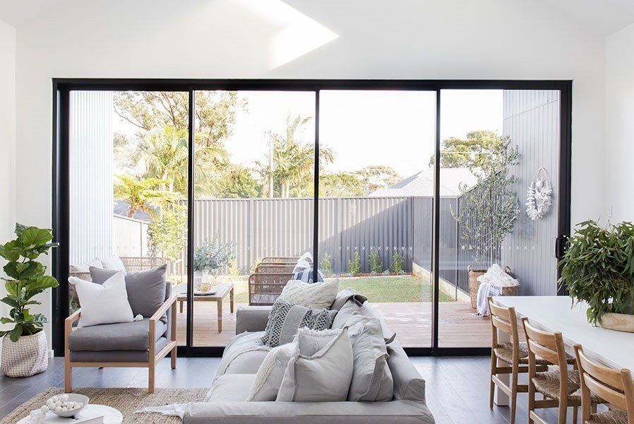 A Living Room With A Couch, Chair, Table And Sliding Glass Doors Leading To A Backyard — Glass 24/7 In Taree, NSW