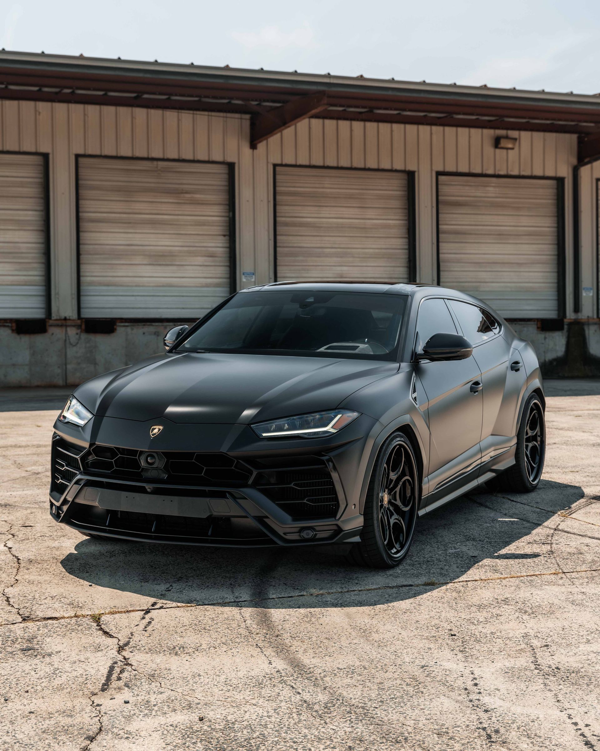 A black lamborghini urus is parked in front of a building.