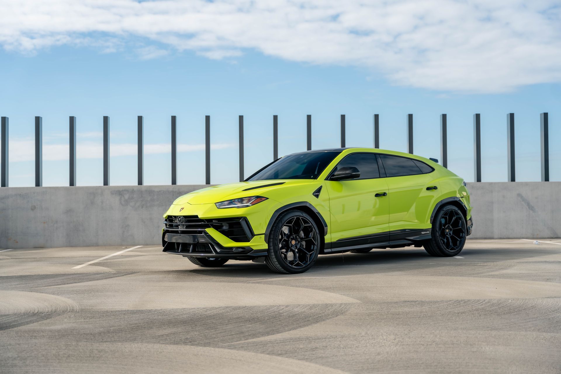 A green lamborghini urus is parked in a parking lot next to a fence.