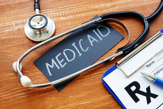 A stethoscope, a prescription pad, and a pen placed on a wooden surface next to a black card labeled 