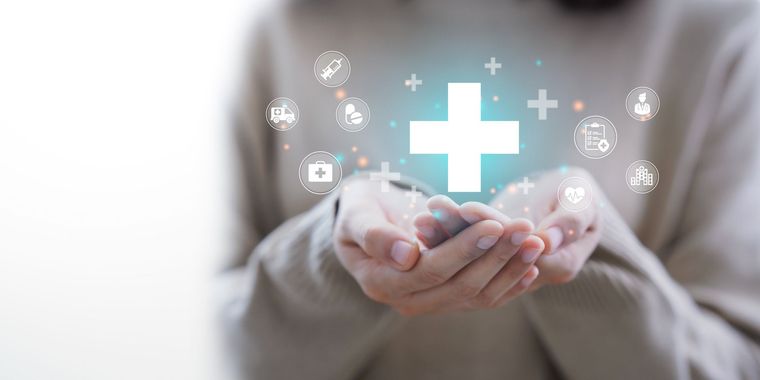 Hands holding a glowing medical cross with health icons in a blurred background