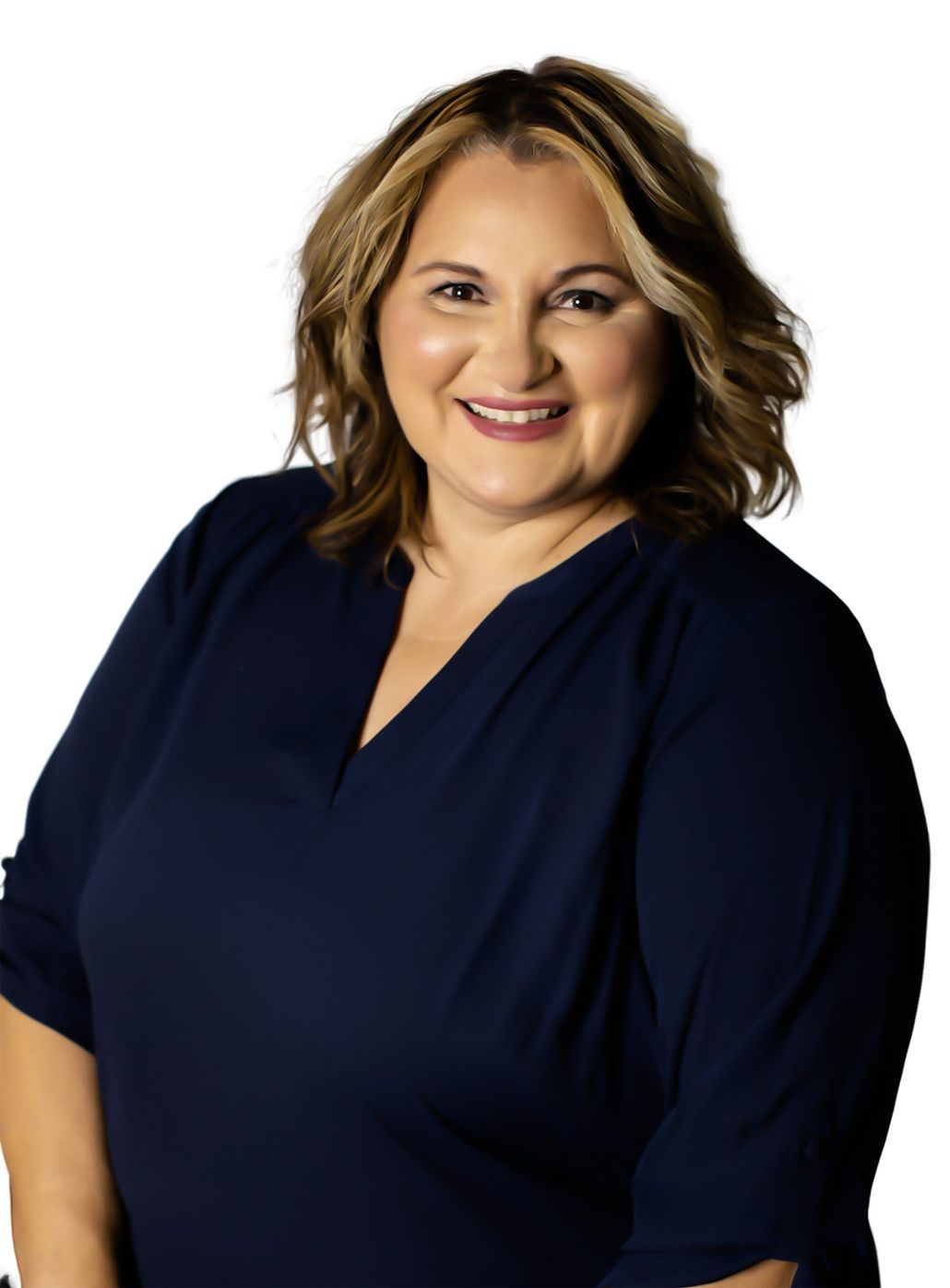 A smiling person with shoulder-length wavy brown hair wearing a dark blue V-neck top against a white background.