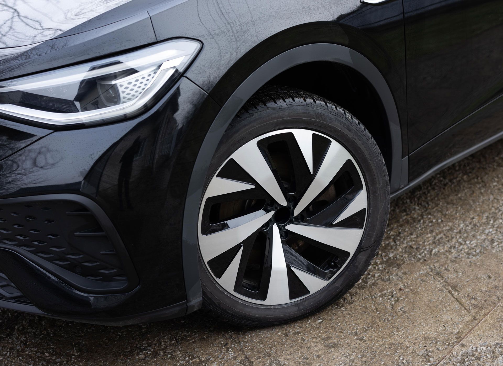 Black car with silver and black wheel. Close-up view of front wheel and headlight.