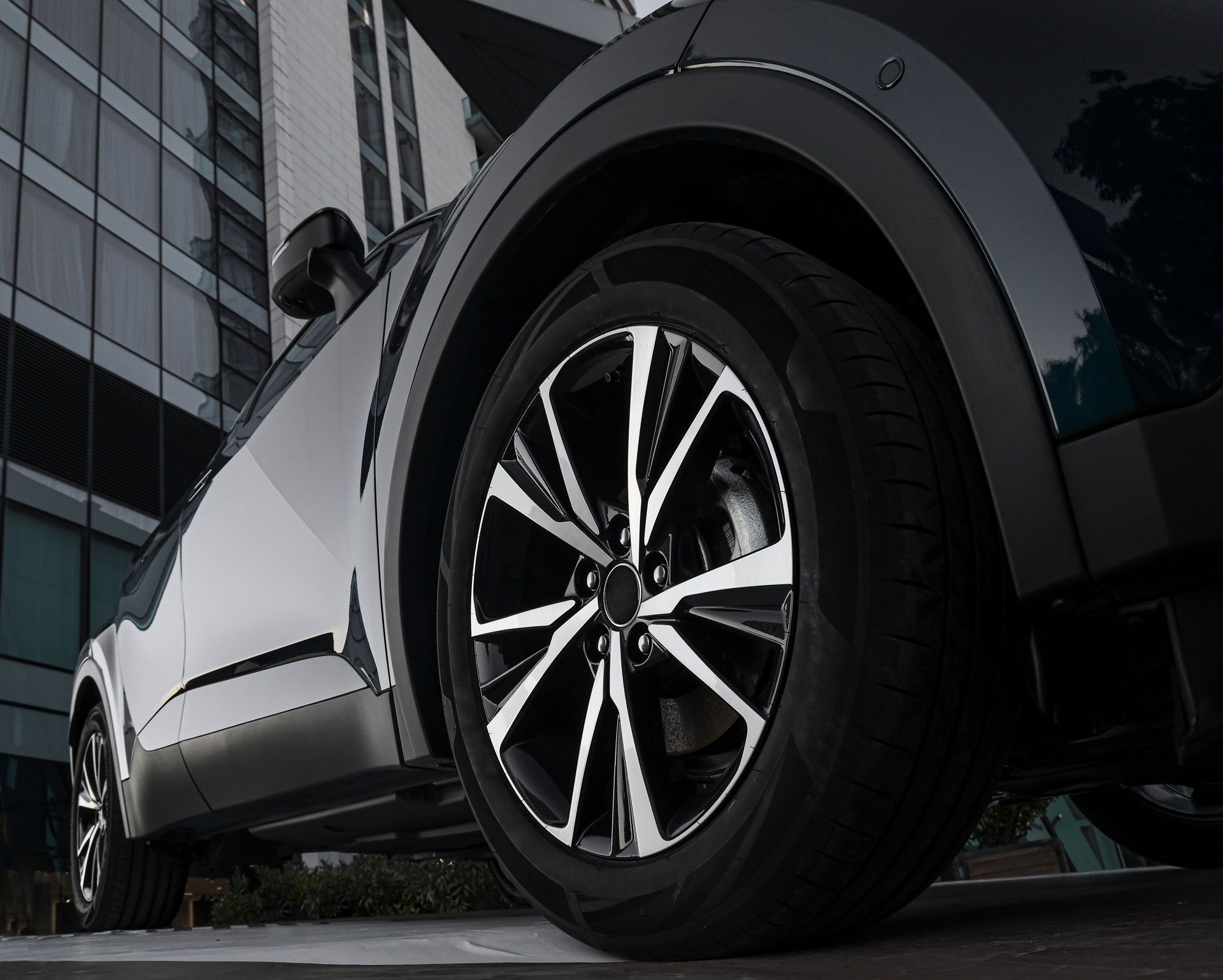 Black and silver car tire, close-up, angled towards a building with reflective windows.