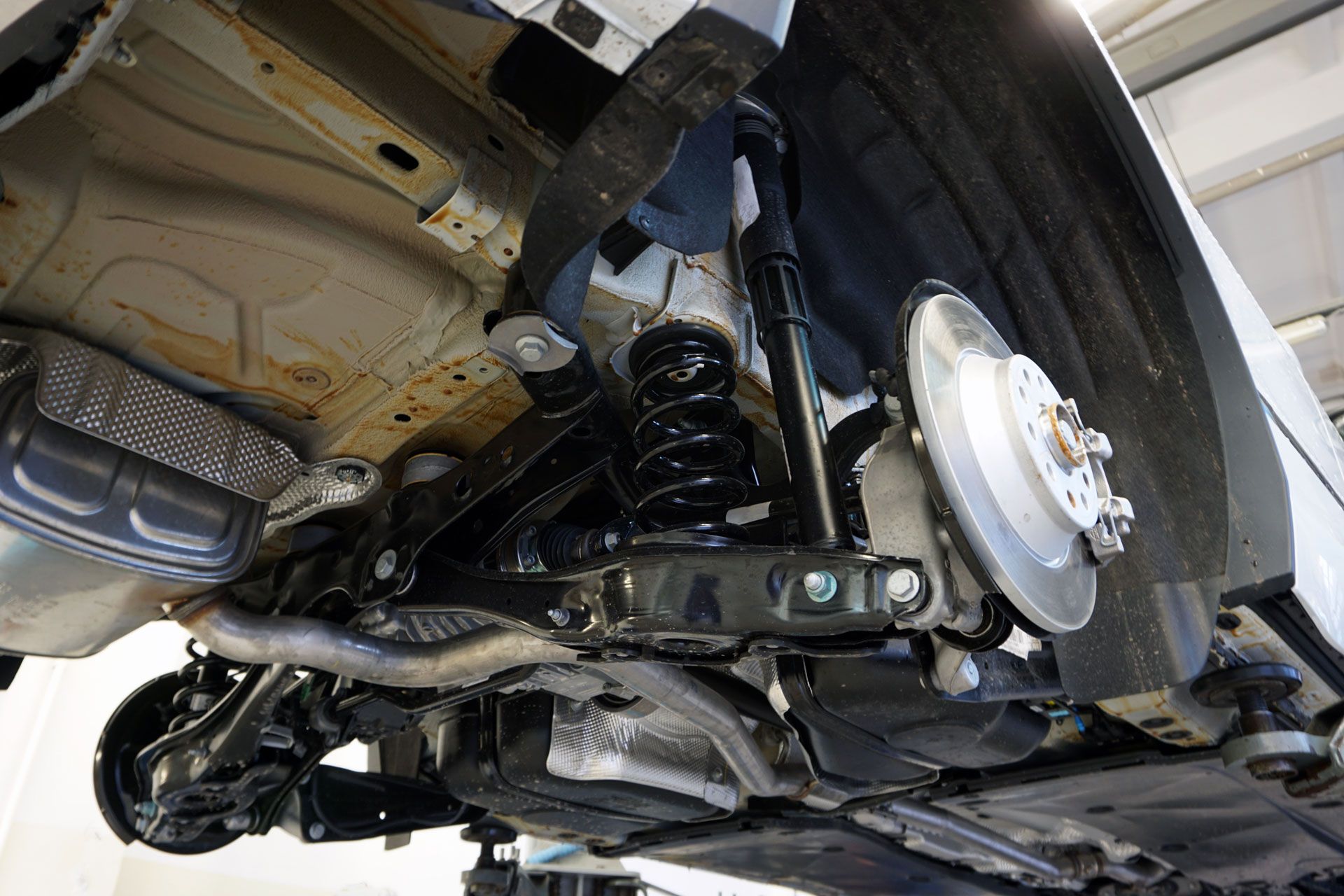 Undercarriage of a vehicle, showing suspension, brakes, and exhaust system. Black and silver components visible.