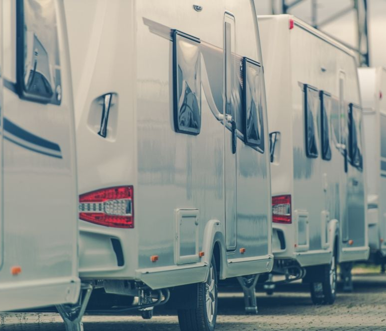 Row of white camper vans parked in a lot, side doors open with blue curtains visible