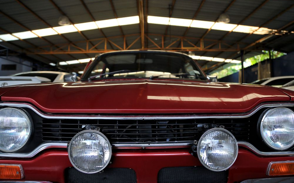 Front view of a maroon classic car with chrome headlights inside a garage