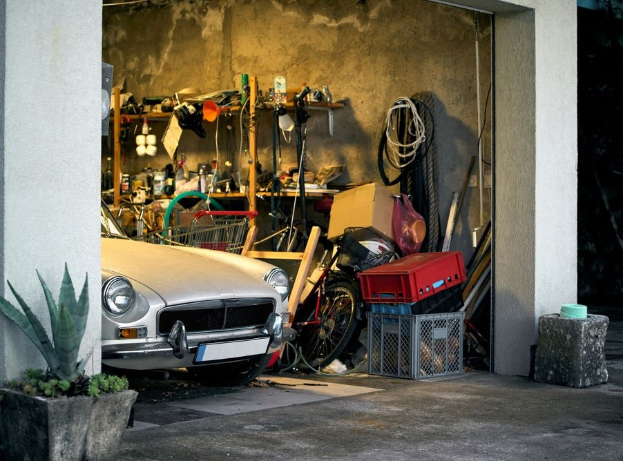 Silver car in a cluttered garage with shelves, tools, and a red storage bin