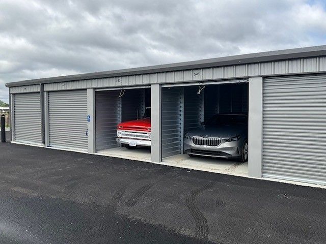 Two cars are parked in a row of garages.
