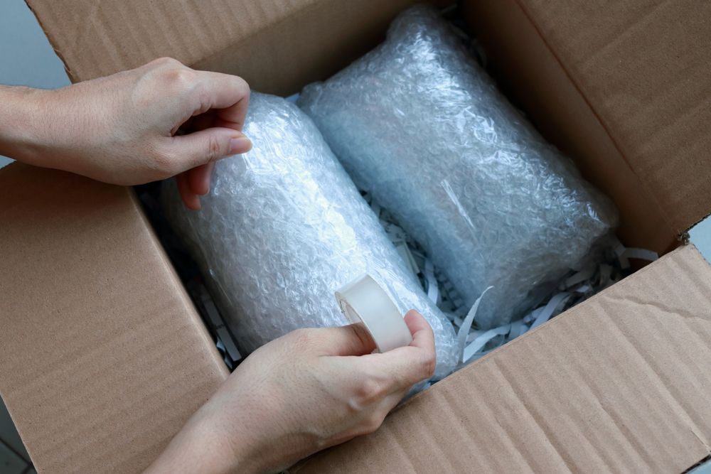 A person is packing a box with bubble wrap and shredded paper.