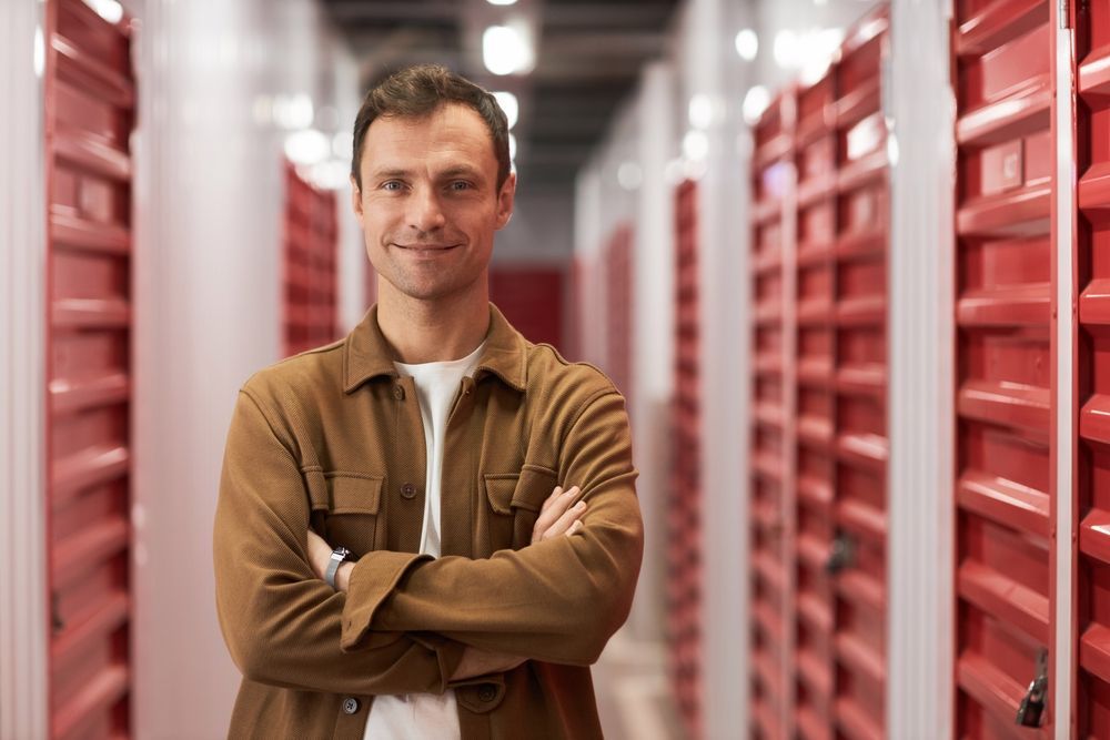 A man is standing in a storage room with his arms crossed.