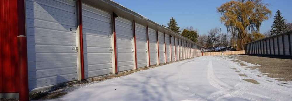 Snow-covered alley beside closed storage unit doors under a blue sky
