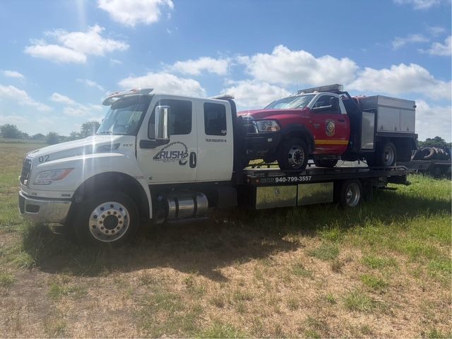 Tow truck carrying a black car, parked on the side of a road.