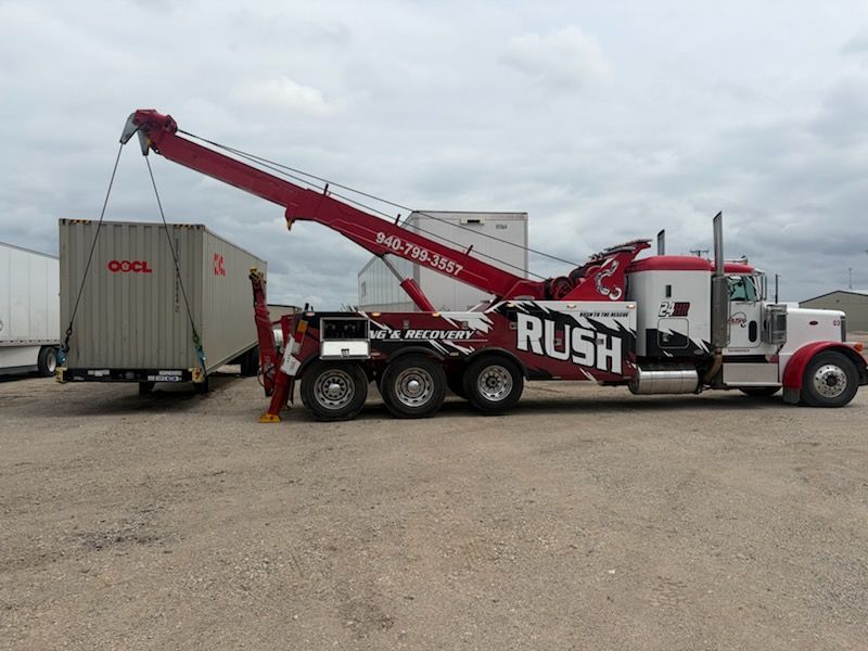 Red heavy-duty tow truck lifting a white shipping container in a gravel lot