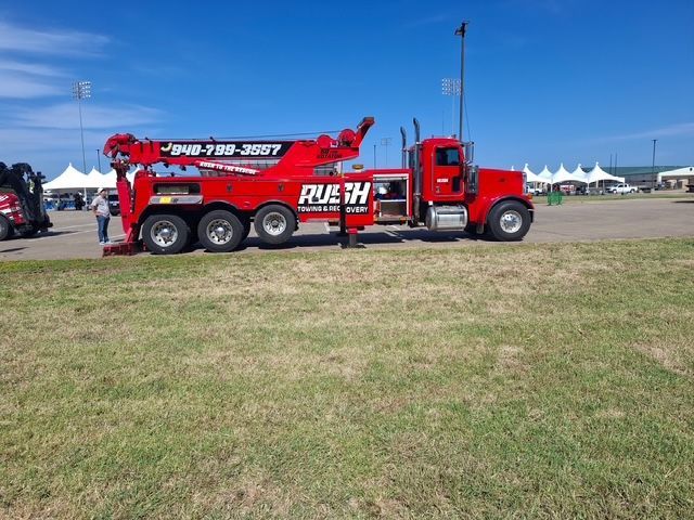 Red tow truck parked on grass at an outdoor event under a blue sky.