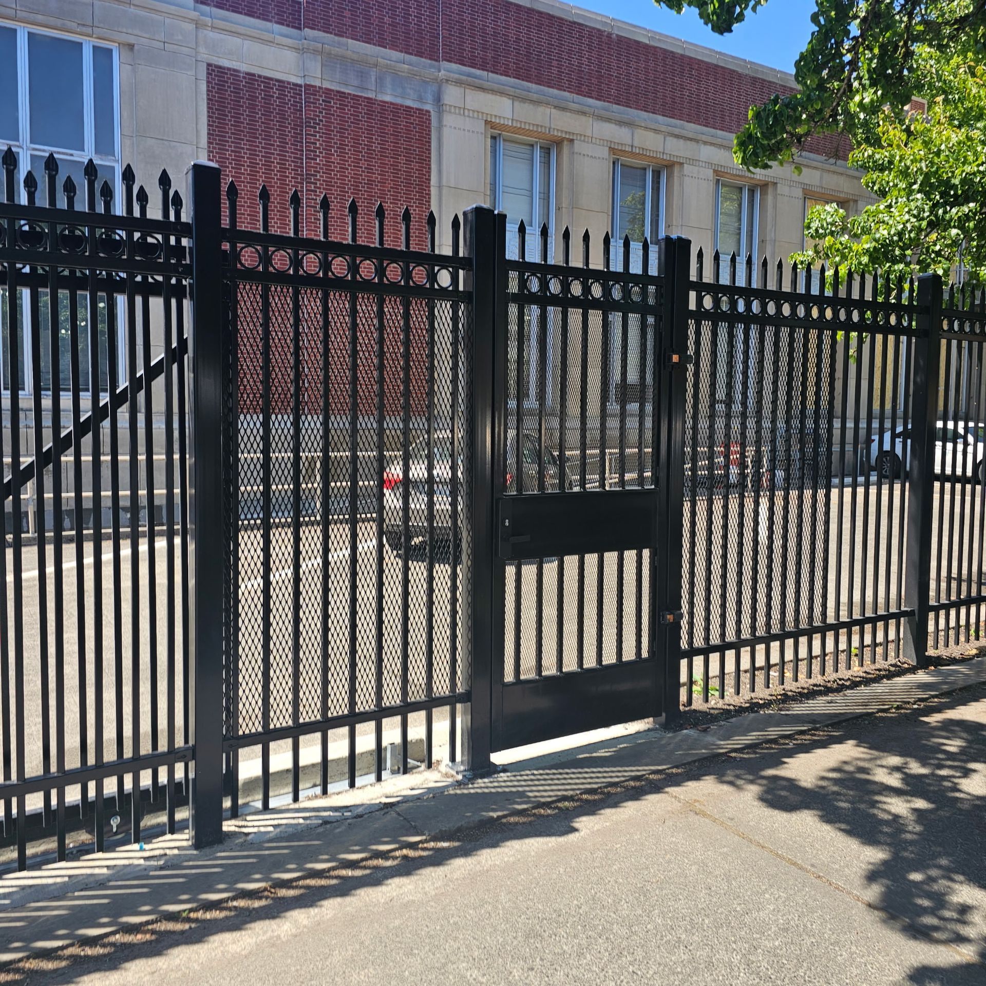 Black metal fence and gate in front of a brick building on a sunny street
