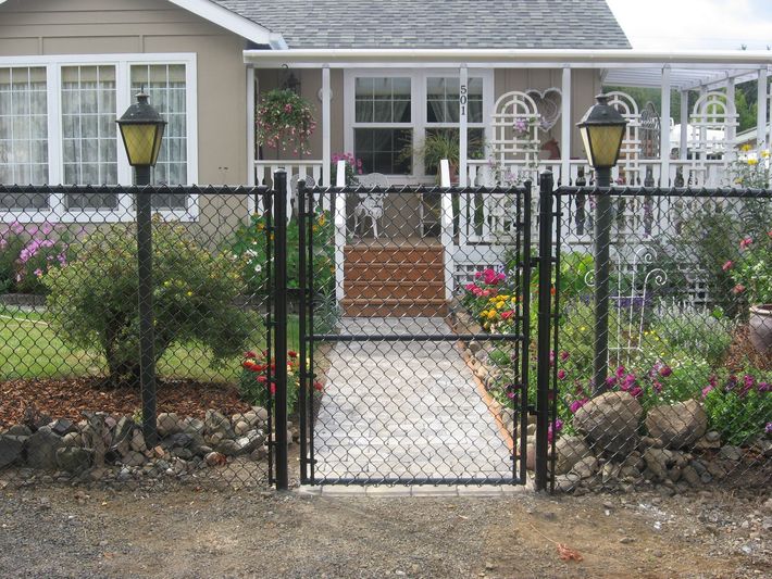 Front yard garden with a black chain-link gate leading to a house porch and flowerbeds