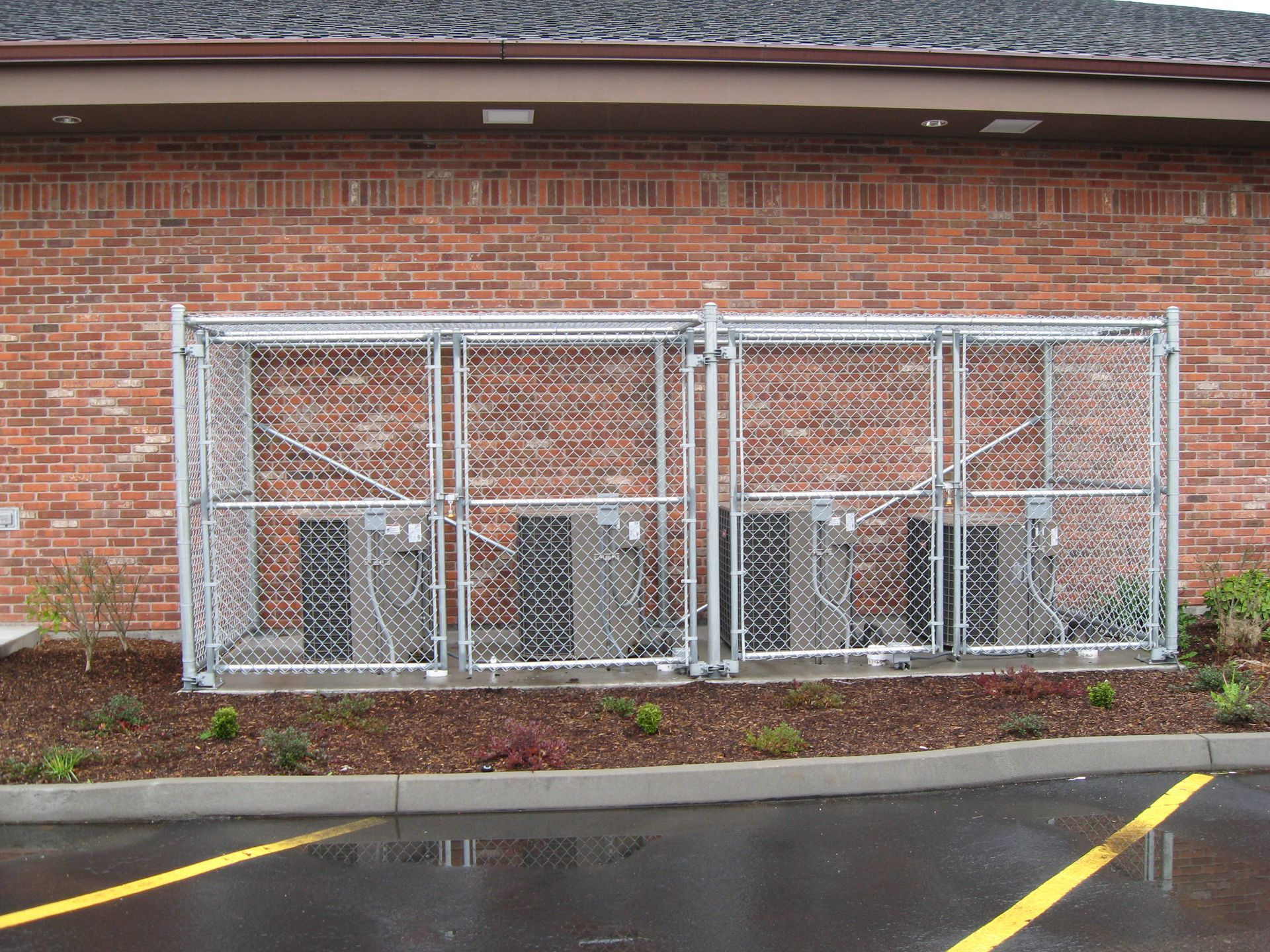 Chain-link kennel against a brick wall, with wet pavement in front and yellow parking lines.
