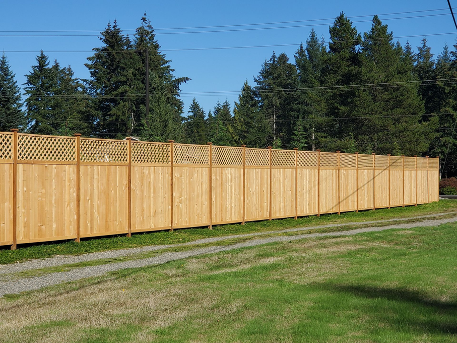 Long wooden privacy fence beside a grassy yard under a clear blue sky with trees in the background